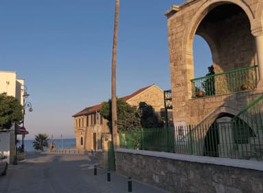 A quiet street in Larnaca with stone buildings and a view of the sea.