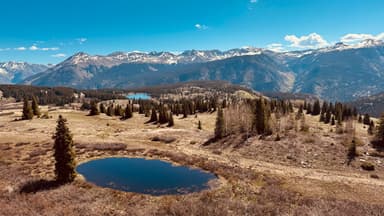 Un paysage de montagnes avec un étang et des arbres sous un ciel bleu.