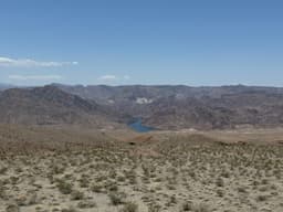 Un paysage désertique avec des montagnes et un lac au loin.