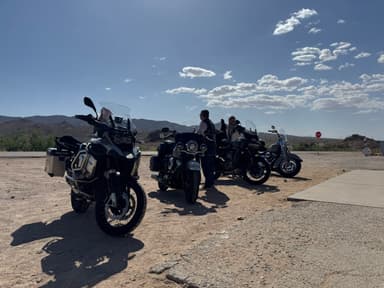 Des motos garées sur une route avec des montagnes en arrière-plan sous un ciel bleu.