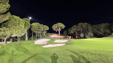 A well-lit golf course at night with sand traps and trees in the background.