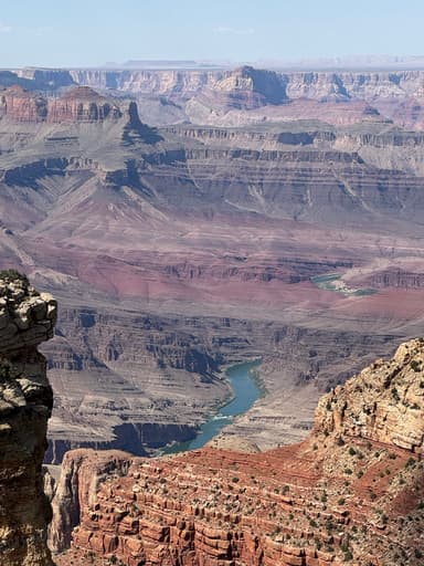 A panoramic view of layered red rock formations and a winding river in a canyon.