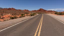 A winding road through red rock formations under a clear blue sky.