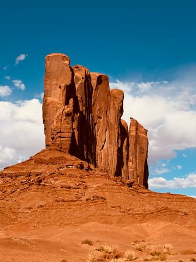 A towering rock formation against a blue sky with clouds in Arizona.