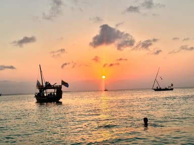 A sunset over the ocean with boats silhouetted against the colorful sky.