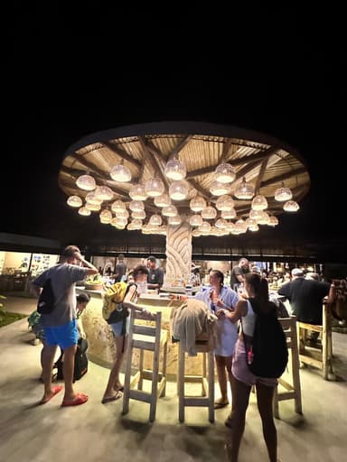 A lively bar scene with people gathered around a unique tree-shaped structure illuminated by hanging lights.