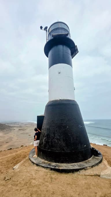 Un phare noir et blanc sur une falaise avec la mer en arrière-plan.