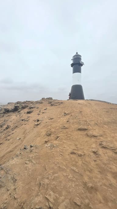 Un phare sur une colline rocheuse sous un ciel nuageux.