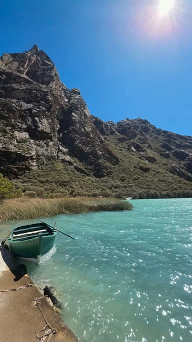 Un bateau vert sur l'eau turquoise avec des montagnes en arrière-plan.