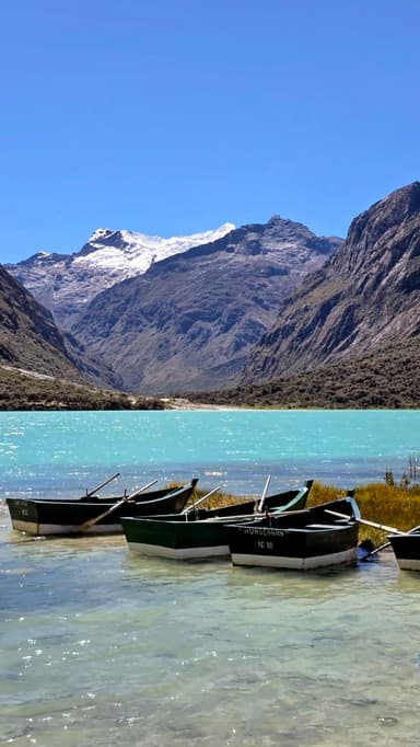 Des bateaux sur un lac turquoise avec des montagnes en arrière-plan.
