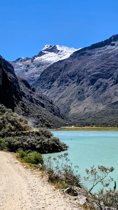 Un paysage de montagne avec un lac turquoise et des sommets enneigés sous un ciel bleu.