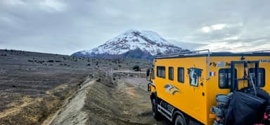 Un camion jaune devant un volcan enneigé sous un ciel nuageux.