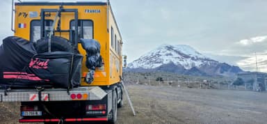 Un camion jaune avec un volcan en arrière-plan sous un ciel nuageux.