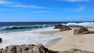 Une plage avec des vagues et des rochers sous un ciel bleu.