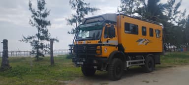 Un camion orange garé près de la plage avec des palmiers en arrière-plan.