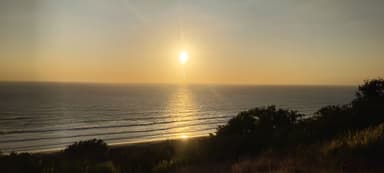 Un coucher de soleil sur l'océan avec des vagues et des collines en arrière-plan.