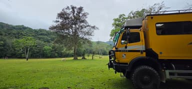 Un camion jaune dans un paysage verdoyant avec des arbres et des collines.