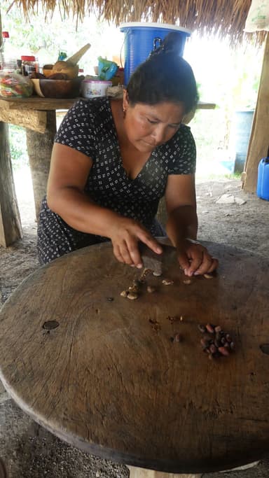 Une femme prépare des ingrédients sur une table en bois dans un environnement naturel.
