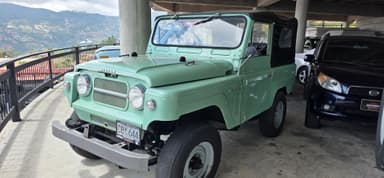 Un véhicule ancien garé sous un bâtiment avec des montagnes en arrière-plan.
