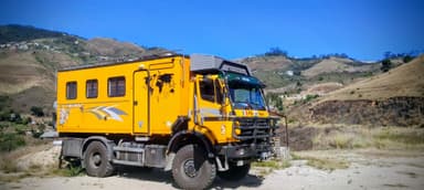 Un camion jaune sur un terrain avec des collines en arrière-plan.