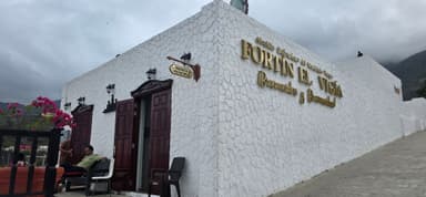 Un bâtiment blanc avec des portes marron et des fleurs roses sous un ciel nuageux.