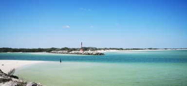 Une plage tranquille avec un phare au loin sous un ciel bleu.