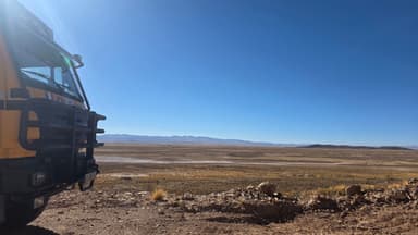 Un paysage désertique avec un camion en premier plan sous un ciel bleu.
