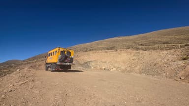 Un véhicule jaune sur une route de terre dans un paysage montagneux.