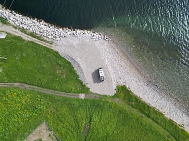 Une vue aérienne d'un véhicule sur une plage de gravier au bord de l'eau.