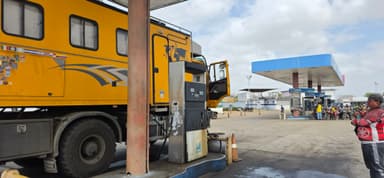 Un camion jaune à une station-service sous un ciel nuageux.