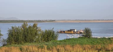 Un paysage fluvial avec un bateau sur l'eau et des arbres au premier plan.