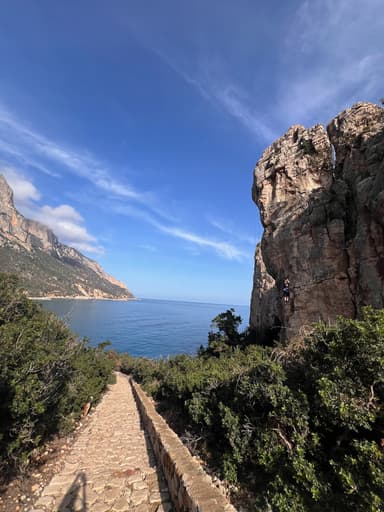Un chemin menant à la mer avec des rochers et des collines sous un ciel bleu.