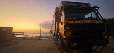 Un camion jaune au coucher de soleil près de la mer.