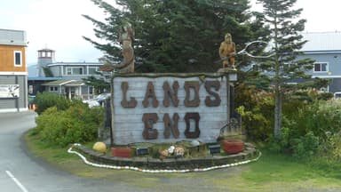 Un panneau en bois avec le texte 'LANDS END' et des sculptures en bois, entouré de verdure.