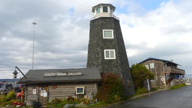 Un phare et un bâtiment en bois au bord de l'eau sous un ciel nuageux.