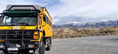 Un camion orange devant des montagnes enneigées sous un ciel nuageux.