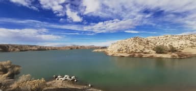 Un paysage de lac entouré de collines sous un ciel nuageux.