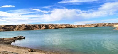 Un paysage de lac entouré de collines sous un ciel bleu.