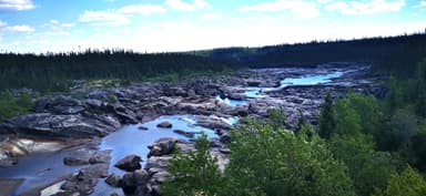 A rocky river landscape with trees under a blue sky.
