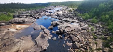 A rocky river landscape with clear water and green trees in the background.
