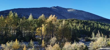Une montagne avec des arbres aux couleurs d'automne sous un ciel bleu.