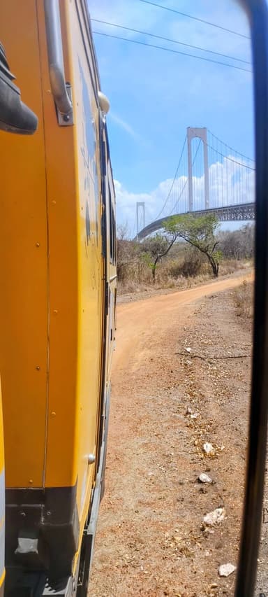 A yellow vehicle on a dirt road with a bridge in the background under a blue sky.
