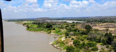 A scenic view of a riverbank with lush greenery under a blue sky with clouds.