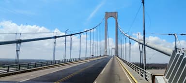 A suspension bridge under a clear blue sky with clouds.