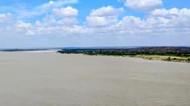 A wide river with green banks under a cloudy sky.