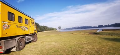 Un camion jaune près d'un lac entouré de verdure et de ciel bleu.