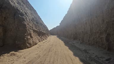 Un chemin de sable entre des falaises rocheuses sous un ciel ensoleillé.