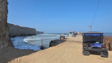 Une vue d'un chemin côtier avec des véhicules et des vagues sous un ciel bleu.