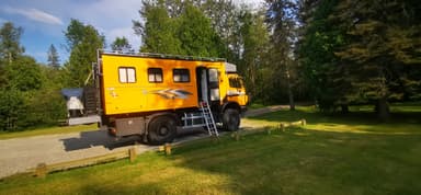 Un camion de voyage orange stationné dans un parc verdoyant.