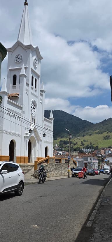 Une église blanche au bord d'une rue avec des montagnes en arrière-plan.